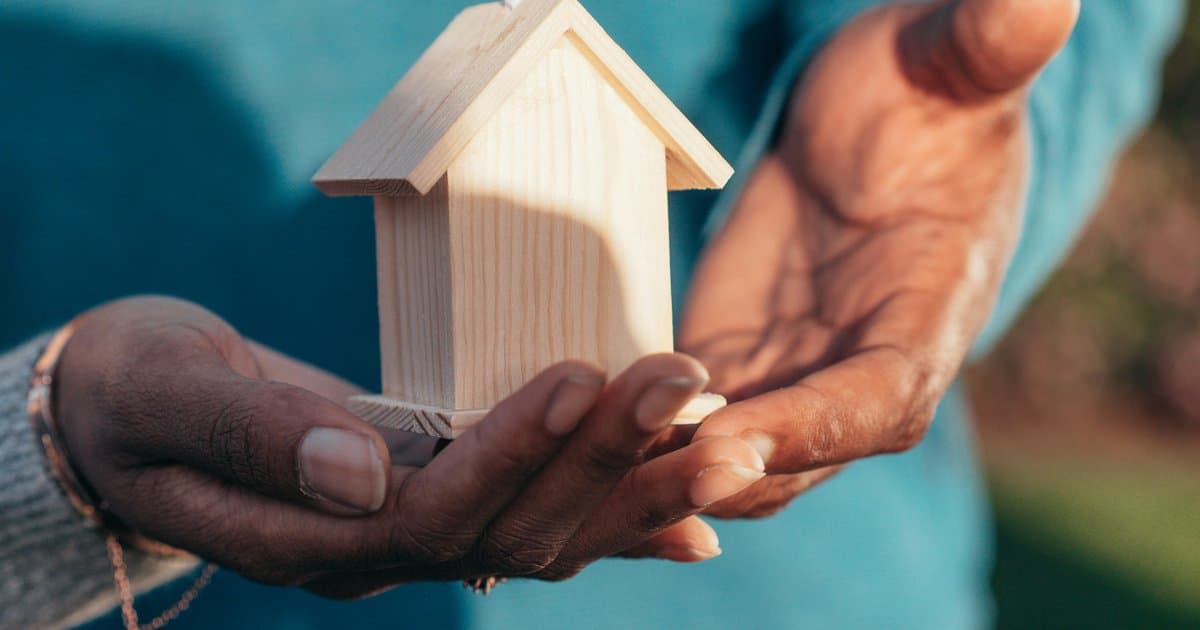 Diverse hands holding wooden house model symbolizing accessibility
