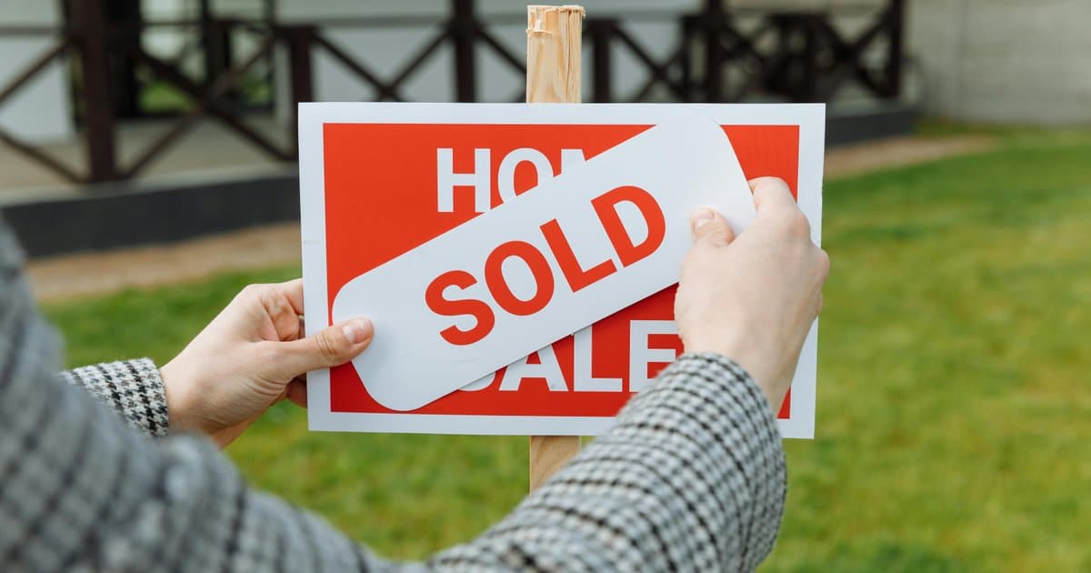 Person placing sold sticker on home for sale sign