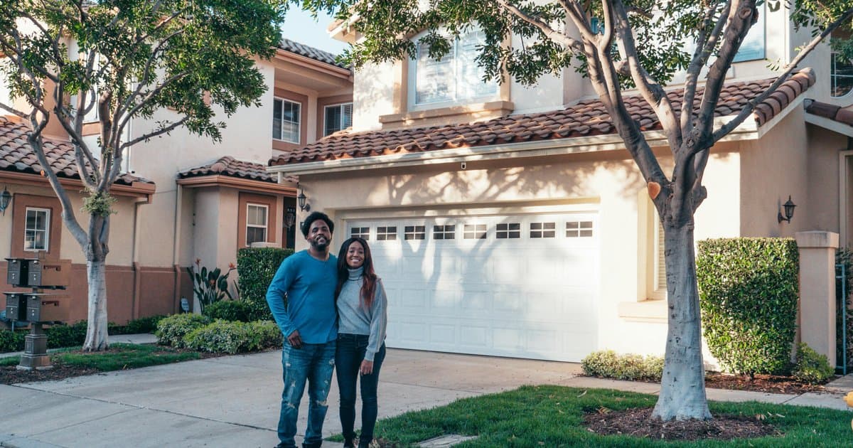 Young couple standing proudly in front of their new home